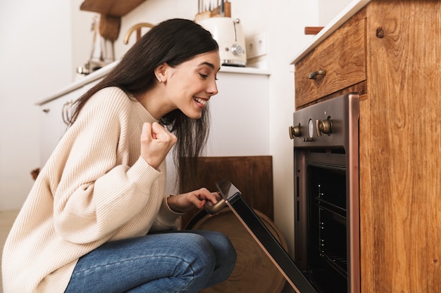 mulher morena sincera cozinhando na cozinha de casa e esperando uma massa caseira com forno aberto