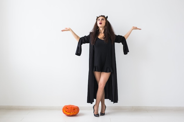 Mulher morena sorridente com maquiagem de halloween, posando com abóbora esculpida sobre fundo claro com espaço de cópia