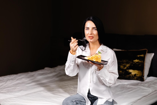 Mulher morena sorridente comendo bolo no quarto em seu apartamento