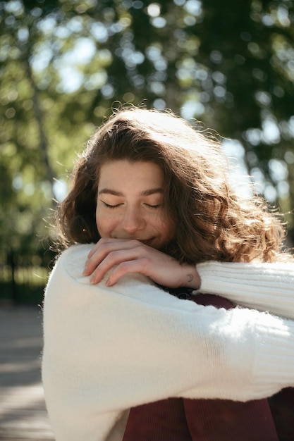 Mulher morena sorridente de olhos fechados sentada no parque