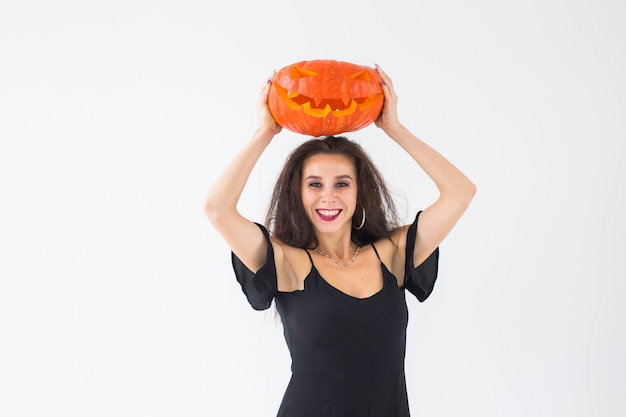 Foto mulher morena sorridente em maquiagem de halloween, posando com abóbora esculpida.