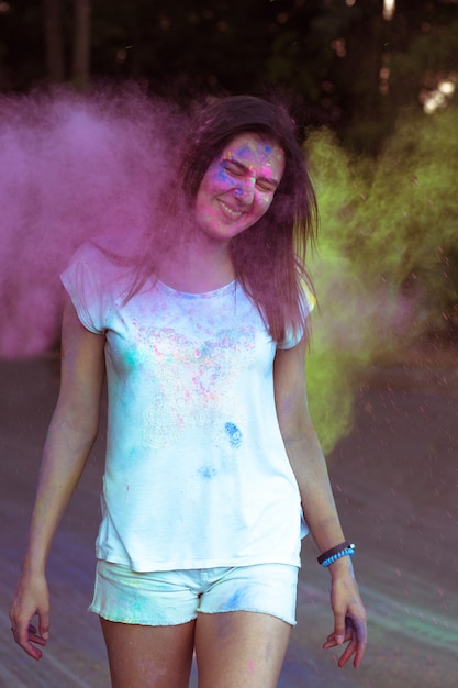 Mulher morena sorridente na natureza coberta com pó de Holi colorido