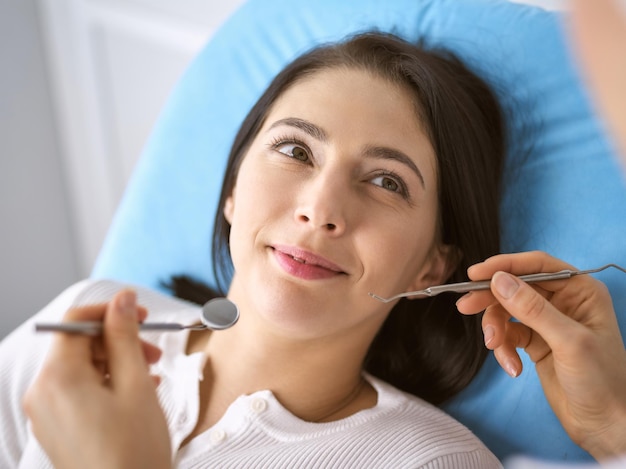 Mulher morena sorridente sendo examinada pelo dentista na clínica odontológica. Mãos de um médico segurando instrumentos odontológicos perto da boca do paciente. Dentes saudáveis e conceito de medicina.