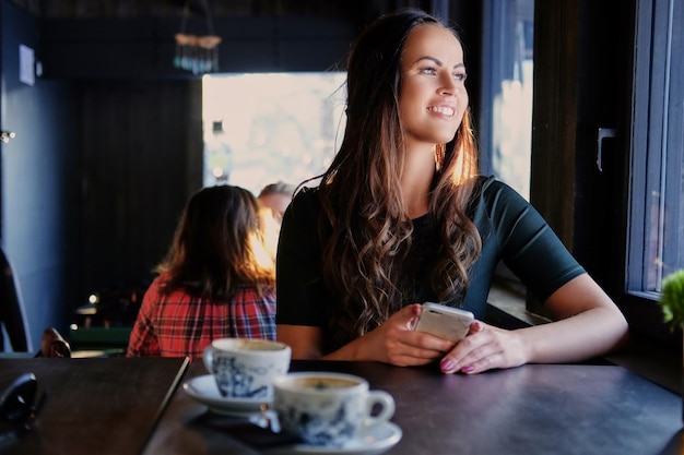 Mulher morena sorridente usando um smartphone em um café.