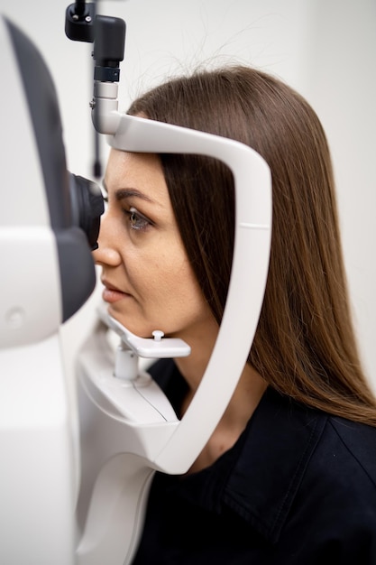 Foto mulher morena tem olhos examinados em uma lâmpada de fenda equipamento moderno para verificação da visão na clínica closeup