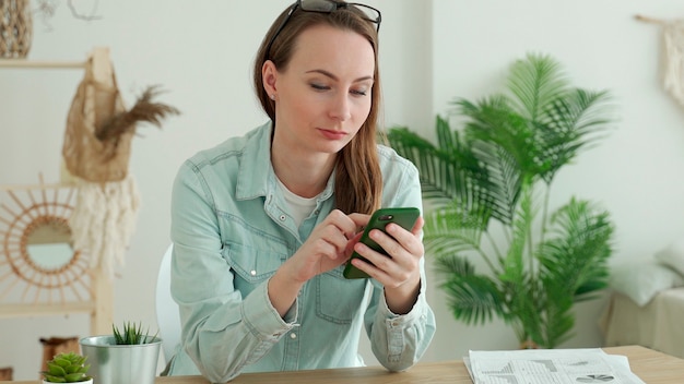 Mulher morena usando smartphone enquanto está sentado no escritório