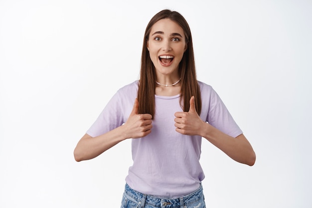 mulher mostra seu apoio, ótimo trabalho, bom gesto de trabalho, polegares para cima e sorriso, encoraja você, esforço de elogio, pisando em branco.