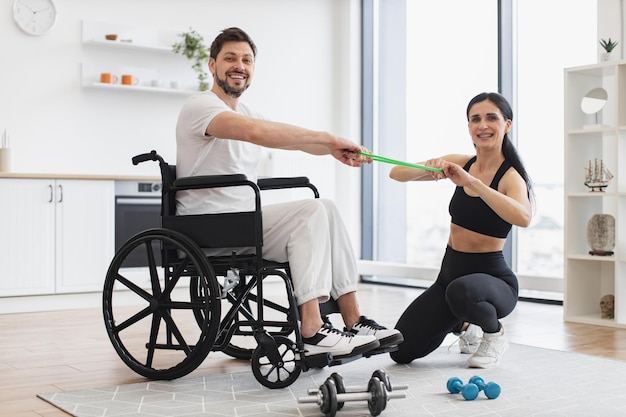 Foto mulher mostrando homem adulto em cadeira de rodas como fazer exercícios com bandas de alongamento