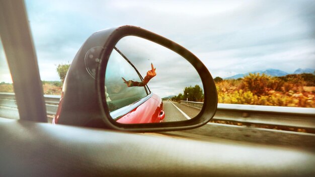 Foto mulher mostrando o dedo médio refletindo no espelho lateral do carro