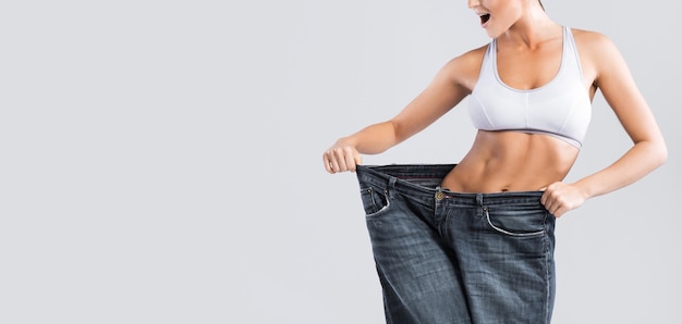 Mulher mostrando resultado após perda de peso usando jeans velhos em fundo cinza