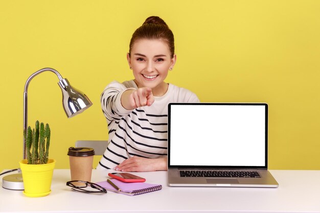 Mulher mostrando tela de laptop vazia para exibição de propaganda apontando o dedo para a câmera