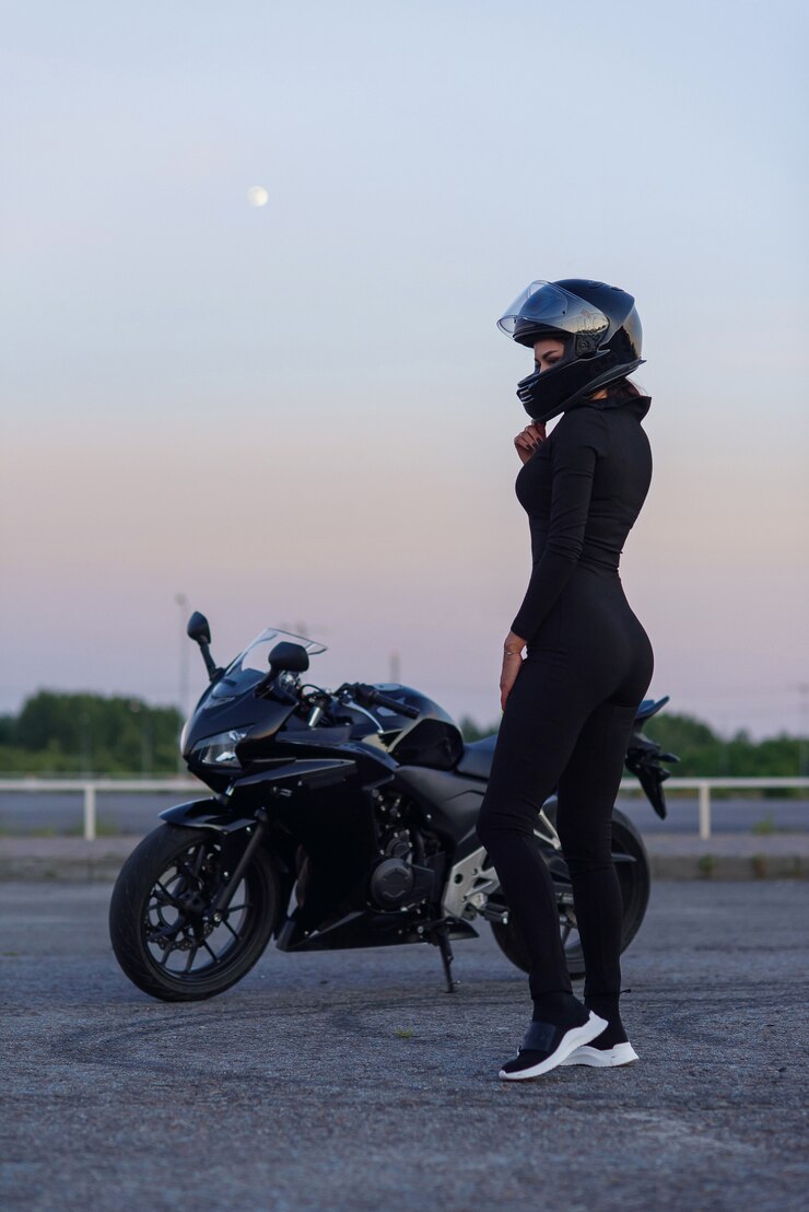 Mulher motociclista na jaqueta de couro preta e capacete facial senta-se perto de moto esportiva elegante no estacionamento urbano. Viajando e conceito de estilo de vida ativo.