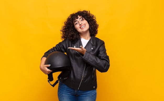 Mulher motociclista sorrindo alegremente, se sentindo feliz e mostrando um conceito no espaço da cópia com a palma da mão