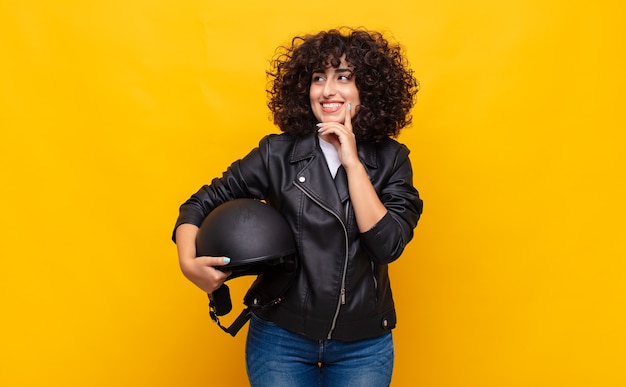 Mulher motociclista sorrindo feliz e sonhando acordada ou duvidando, olhando para o lado