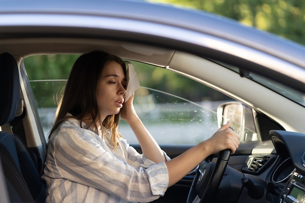 Mulher motorista sentindo calor durante uma onda de calor em um carro sofrendo de calor limpa o suor da testa