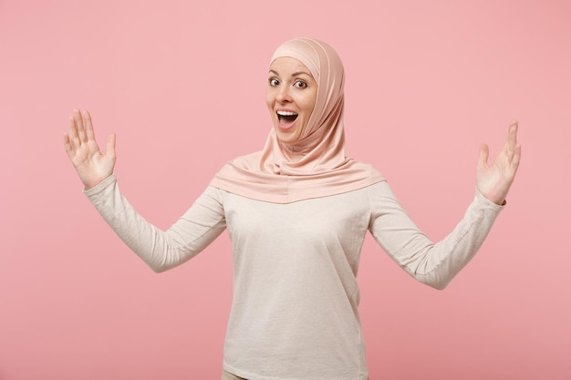 Mulher muçulmana árabe animada em roupas leves hijab posando isolado no fundo rosa. conceito de estilo de vida religioso de pessoas. mock up espaço de cópia. gesticulando demonstrando tamanho com espaço de trabalho horizontal.