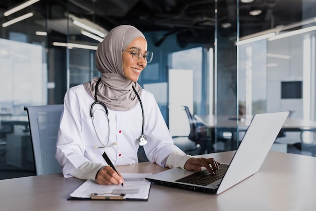 Mulher muçulmana árabe em médico hijab trabalhando no escritório de clínica moderna com médico laptop em papel