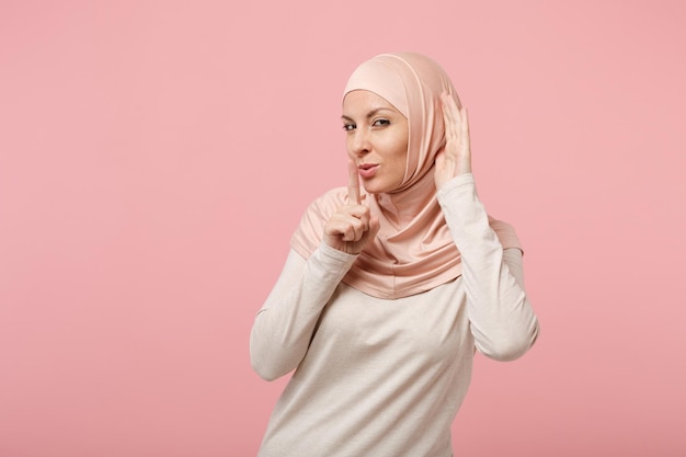 Mulher muçulmana árabe em roupas leves hijab isoladas no fundo rosa. Conceito de estilo de vida religioso de pessoas. Mock up espaço de cópia. Dizendo silêncio fique quieto com o dedo nos lábios gesto de shhh, tente ouvir você.