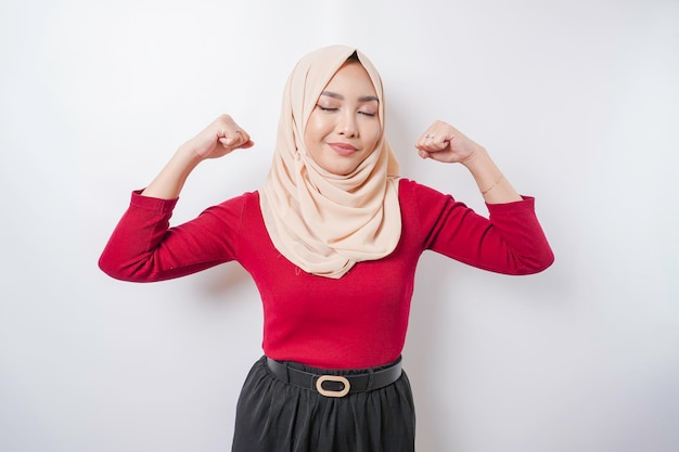 Mulher muçulmana asiática animada usando um hijab mostrando um gesto forte levantando os braços e os músculos sorrindo com orgulho