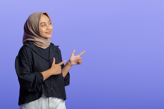 Mulher muçulmana asiática apontando para o espaço de cópia isolado