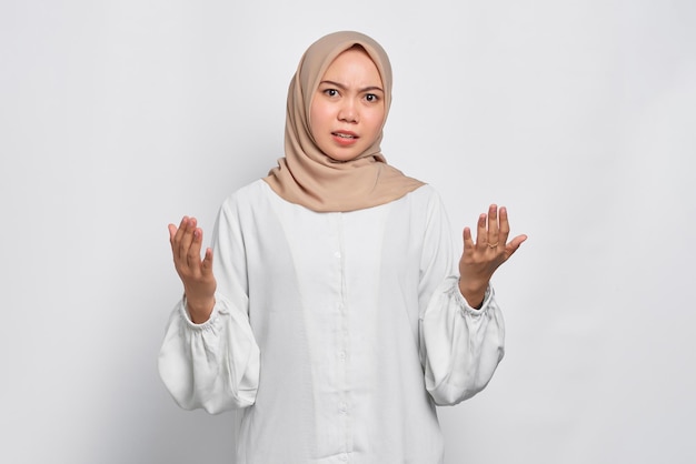 Mulher muçulmana asiática confusa espalha as mãos lateralmente sente dúvida ao fazer escolha isolada sobre fundo branco