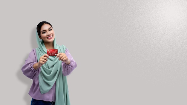 Mulher muçulmana asiática em um lenço na cabeça segurando um cartão de crédito