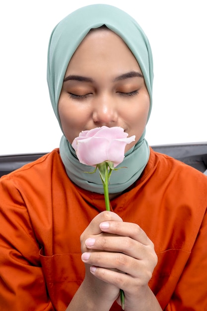 Mulher muçulmana asiática em um lenço na cabeça sentado em uma mala enquanto segura uma flor rosa