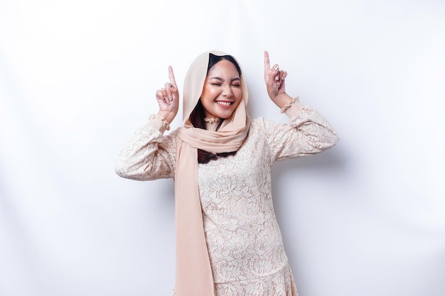 Mulher muçulmana asiática excitada usando hijab apontando para o espaço da cópia acima dela isolado por fundo branco
