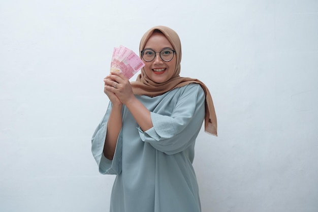 Mulher muçulmana asiática feliz segurando dinheiro em rupia indonésia