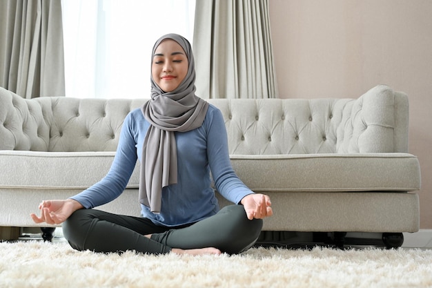 Mulher muçulmana asiática milenar pacífica praticando ioga concentrada meditando