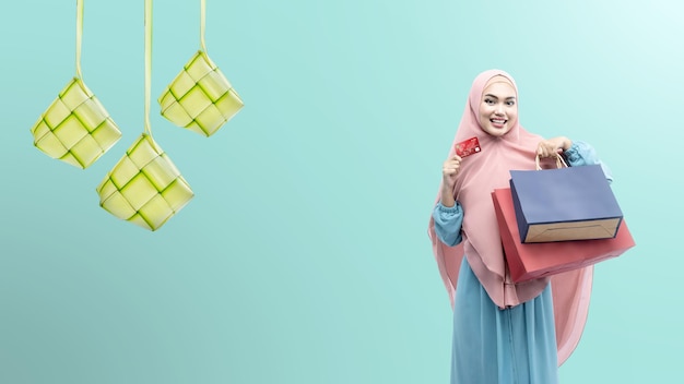 Mulher muçulmana asiática no véu segurando o cartão de crédito e sacolas de compras