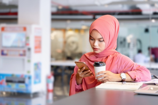 Mulher muçulmana asiática nova bonita no hijab cor-de-rosa e vestuário desportivo que trabalha com portátil e relatório comercial no trabalho criativo.