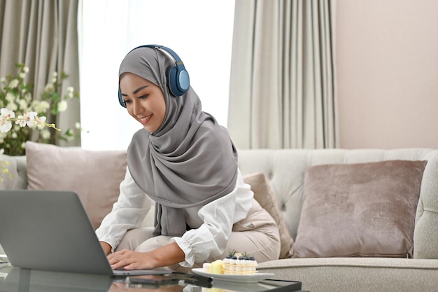 Mulher muçulmana asiática usando fones de ouvido e usando computador portátil