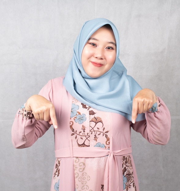 Mulher muçulmana asiática vestindo camisa rosa e lenço azul está promovendo com as duas mãos apontando para baixo