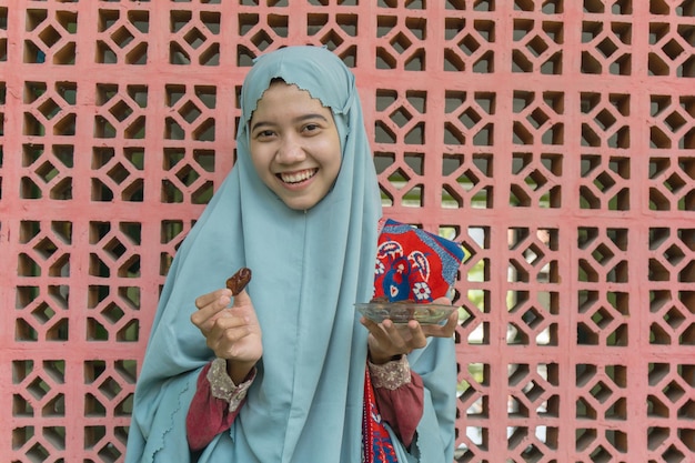 mulher muçulmana asiática vestindo hijab segurando um prato de tâmaras nas mãos para quebrar o jejum