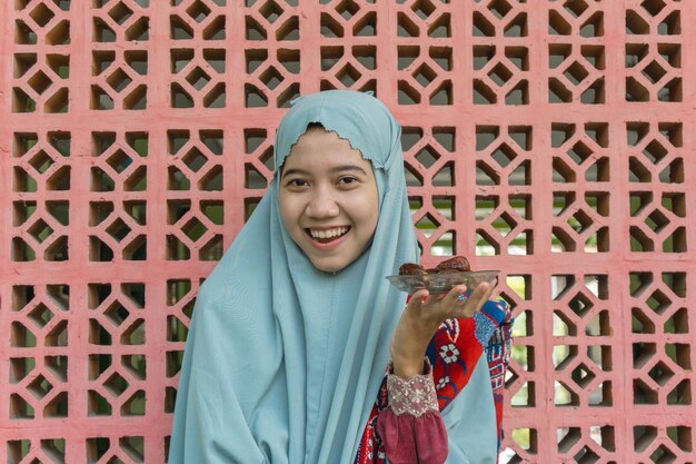 Foto mulher muçulmana asiática vestindo roupas de oração segurando datas com fundo de ornamento islâmico