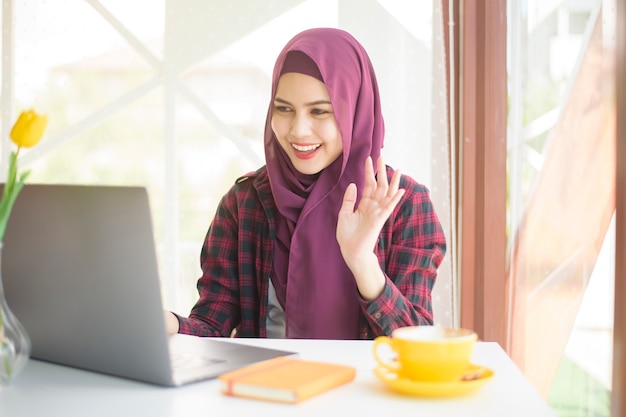 Mulher muçulmana com hijab está trabalhando com o computador portátil na cafeteria