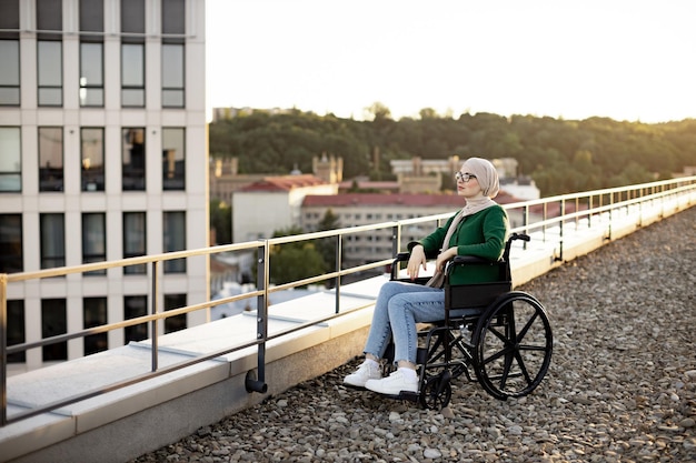 Foto mulher muçulmana com problemas de mobilidade sonhando acordada no terraço