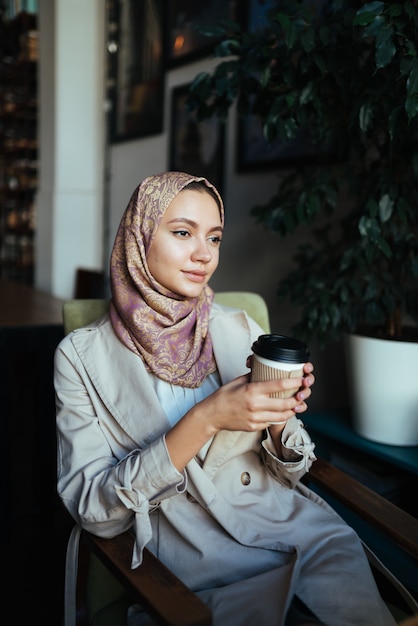 Mulher muçulmana com um olhar atencioso sentada em um café com café na mão