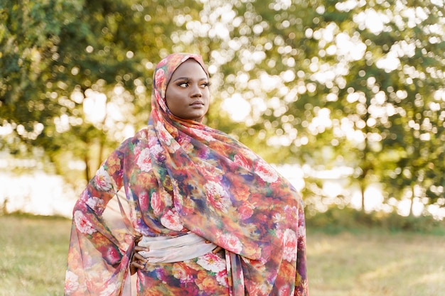 Mulher muçulmana de etnia africana usando o tradicional hijab colorido parece do lado direito do prado verde