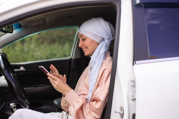 Mulher muçulmana está sentada no carro moderno e falando pelo celular