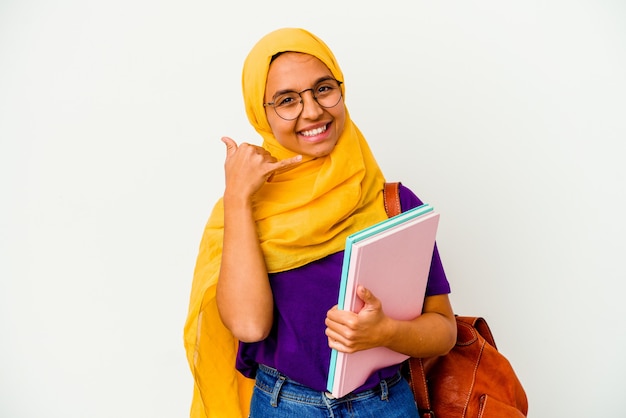 Foto mulher muçulmana jovem estudante vestindo um hijab isolado no fundo branco, mostrando um gesto de chamada de telefone móvel com os dedos.