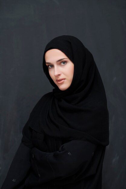 Mulher muçulmana jovem moderna em abaya preto. Menina árabe vestindo roupas tradicionais e posando na frente do quadro negro. Representando o estilo de vida árabe moderno e rico