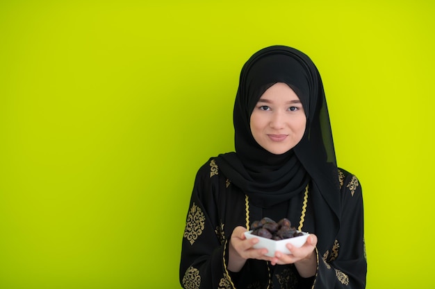 mulher muçulmana moderna segurando um prato cheio de tâmaras doces no horário iftar no ramadan kareem conceito de comida saudável islâmica fundo verde ufo