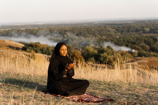 Mulher muçulmana negra rezando no tapete. Solat orando na bela colina. Salah reza tradicional.
