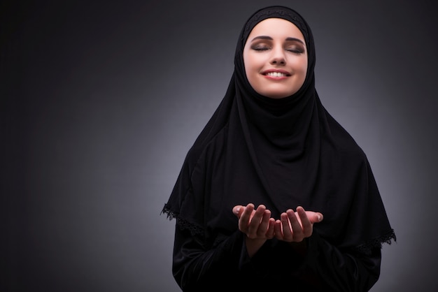 Mulher muçulmana no vestido preto contra o fundo escuro