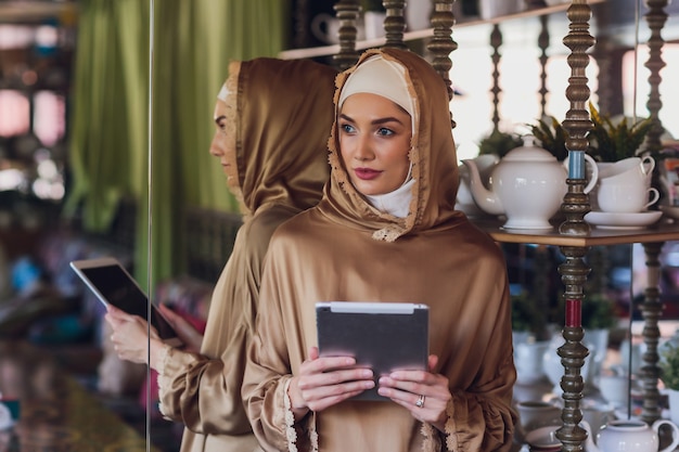 Mulher muçulmana pensativa olhando para um tablet digital