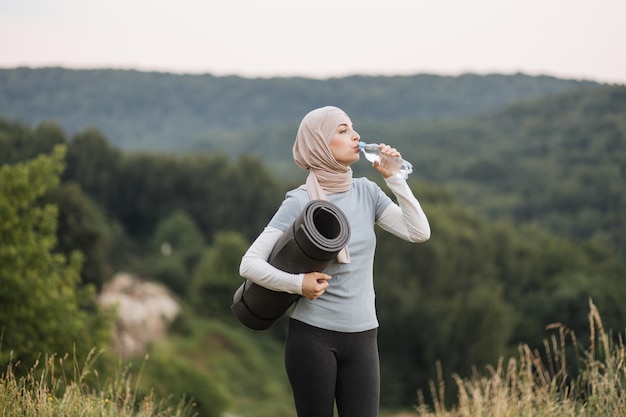 Mulher muçulmana relaxante e refrescante após a prática de ioga ao ar livre