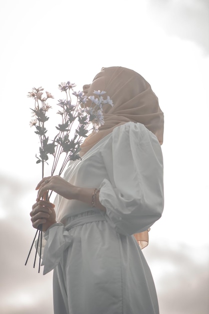 Mulher muçulmana segurando flor em pé olhando para o céu