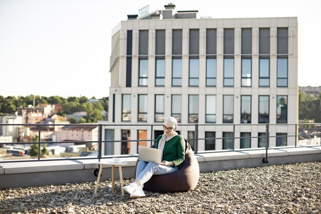Mulher muçulmana trabalhando no computador enquanto está sentado no terraço